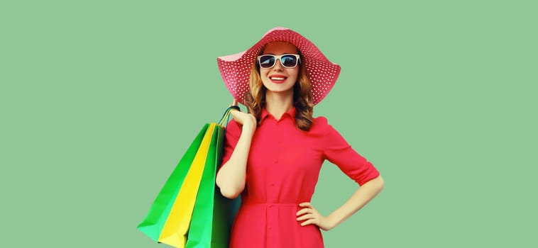 Portrait of beautiful happy smiling young woman model posing with colorful shopping bags wearing summer straw hat, dress on green studio background