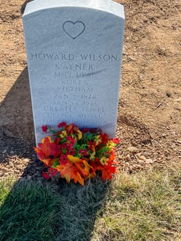 Denver, Colorado, USA-November 12, 2023-A gravestone at a cemetery marking the final resting place of Howard Wilson Kayner, a Major in the US Army who served in Korea and Vietnam. The gravestone is adorned with a vibrant floral tribute, adding a touch of color and remembrance.