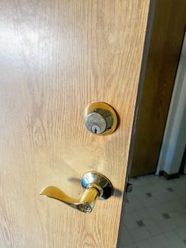 Denver, Colorado, USA-November 25, 2023-A close-up view of a polished brass door handle and matching deadbolt on a wooden door. The shiny brass fixtures add a touch of elegance and security to the doors natural wood grain.