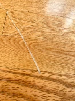 Detailed close-up image showcasing a visible scratch on a hardwood floor. The image highlights the texture and grain of the wood along with the imperfection, illustrating the common wear and tear in residential interiors.