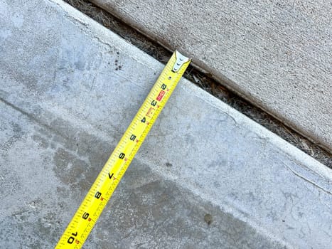 Close-up of a measuring tape placed along a concrete joint in a driveway. The image captures the process of assessing the width of the joint for repair work, highlighting the attention to detail in home maintenance.