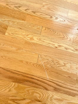 Detailed close-up image showcasing a visible scratch on a hardwood floor. The image highlights the texture and grain of the wood along with the imperfection, illustrating the common wear and tear in residential interiors.