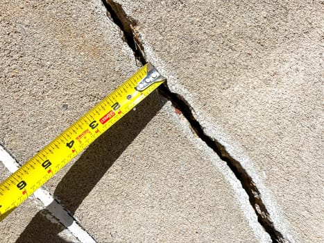 Close-up of a measuring tape placed along a concrete joint in a driveway. The image captures the process of assessing the width of the joint for repair work, highlighting the attention to detail in home maintenance.