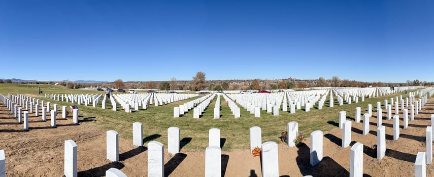 Denver, Colorado, USA-November 12, 2023-A wide panoramic shot capturing the expansive Fort Logan Cemetery in Denver. Rows of white headstones stand in orderly formation under a clear blue sky, reflecting the solemnity and reverence of the resting place.