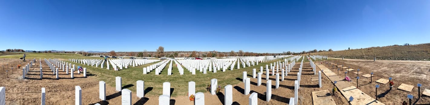 Denver, Colorado, USA-November 12, 2023-A wide panoramic shot capturing the expansive Fort Logan Cemetery in Denver. Rows of white headstones stand in orderly formation under a clear blue sky, reflecting the solemnity and reverence of the resting place.