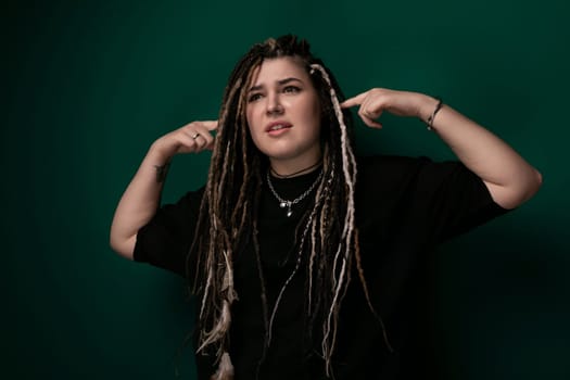 A woman with dreadlocks stands confidently in front of a vibrant green background, her hair flowing freely. She looks directly at the camera, exuding a sense of strength and individuality.