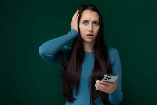 A woman holding a cell phone in her hand, looking at the screen with a focused expression. She is standing outdoors, with trees in the background.