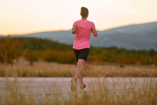 A determined athlete runs confidently under the sun, surrounded by stunning natural scenery, showcasing strength and resilience in her pursuit of fitness