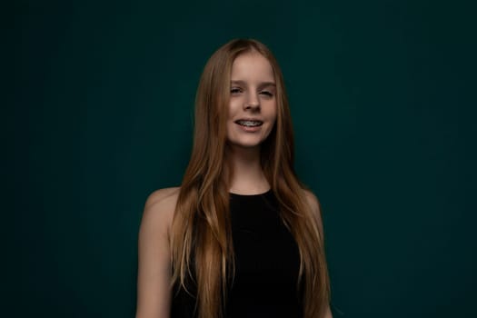 A woman with long red hair standing confidently in front of a vibrant green background. Her flowing hair contrasts beautifully with the verdant backdrop.