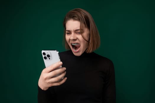 A woman is holding a cell phone with her mouth open in surprise or shock. She appears to be engaging in a conversation or reacting to something on the phone.