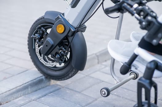 A faceless woman in a wheelchair with an assistive device for manual control. Electric handbike