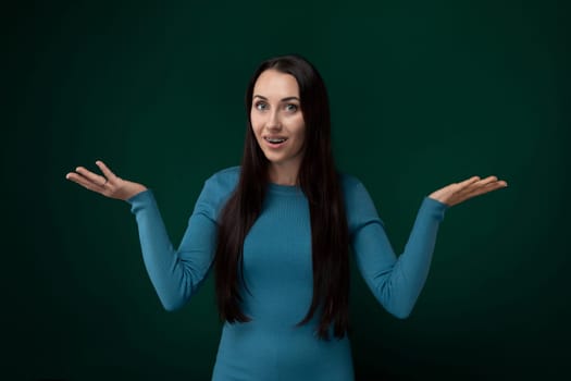 A woman in a blue dress stands with her hands extended in front of her. She appears to be gesturing or expressing something, her body language indicating openness or readiness.