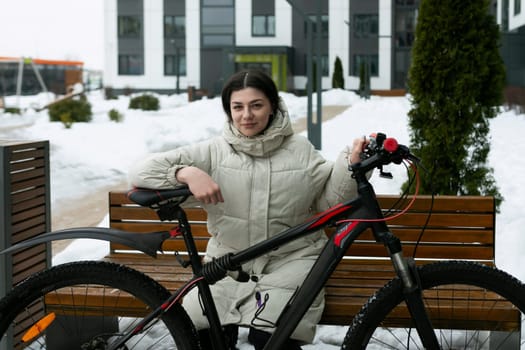 A woman is seated on a bench next to a parked bicycle. She appears to be resting or taking a break. The bike is leaning against the bench, suggesting it belongs to her.