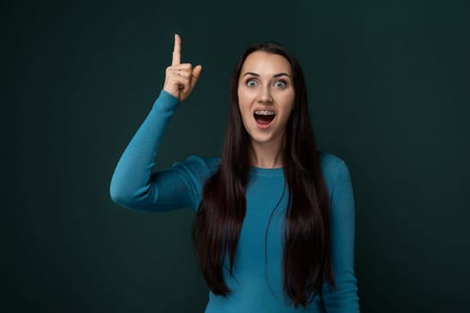 A woman in a blue shirt is pointing at an object or direction with her hand. She appears focused and engaged in the action, potentially indicating interest or significance towards the pointed object.