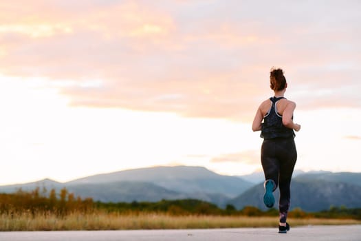 A determined athlete runs confidently under the sun, surrounded by stunning natural scenery, showcasing strength and resilience in her pursuit of fitness