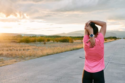 A lone athlete is captured stretching gracefully against the backdrop of a stunning sunset, her silhouette a testament to dedication and resilience after an intense run