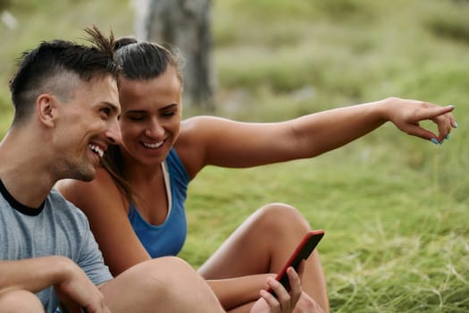 A romantic couple sits in the forest, browsing new running routes on their smartphone, embracing the beauty of nature as they plan their next outdoor adventure together