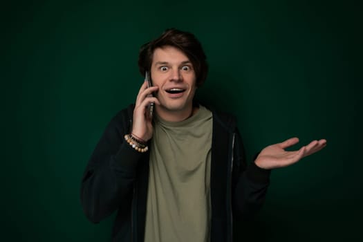 A man standing outdoors, holding a cell phone to his ear with a surprised expression on his face. He appears to be engaged in a conversation that has caught him off guard.