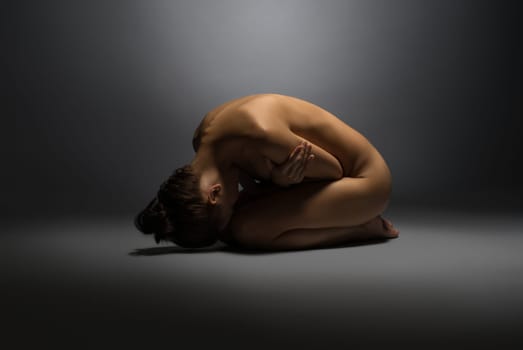 Concept of vulnerability. Naked woman lying on floor, hugging herself