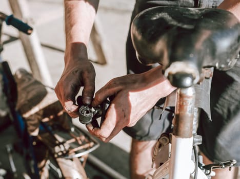 One young unrecognizable man is repairing a bicycle with two dirty hands while standing on the street on a sunny summer day, close-up side view. Bicycle repair concept.