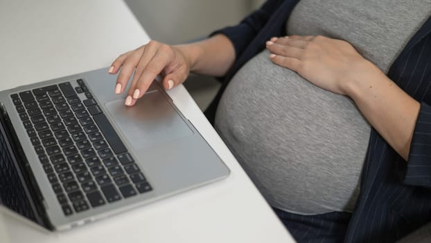 A pregnant woman works on a laptop in the office. Close-up of the tummy