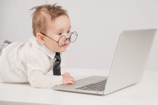 Cute baby in glasses and suit working on laptop