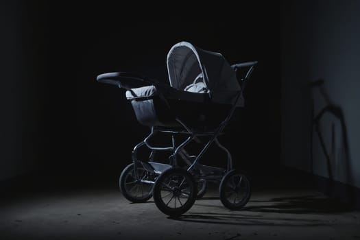 Bathed in a spotlight's cold gleam against an otherwise empty wall, stands an antique baby stroller. This black and white image captures the eerie loneliness and nostalgic overtones imprinted in its silhouette and the surrounding quiet.