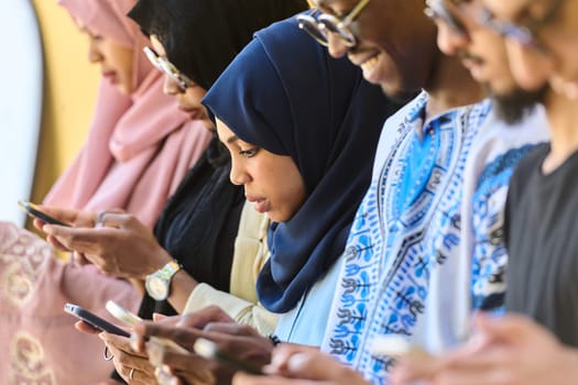 A diverse group of teenagers standing together against a wall, engrossed in their smartphones, showcasing modern connectivity and social interaction.