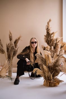 A woman photographer, a blonde with a camera, seriously with sunglasses in the production studio. Wearing a black clothes on a brown background