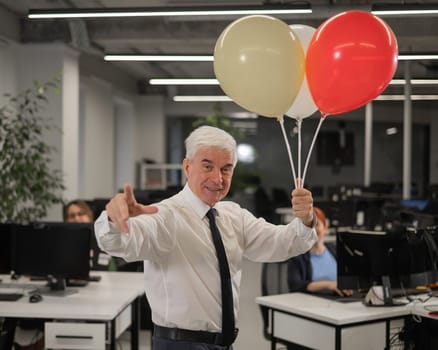 Portrait of a cheerful mature business man holding balloons in the office