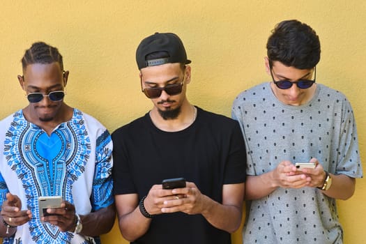 A diverse group of teenagers standing together against a wall, engrossed in their smartphones, showcasing modern connectivity and social interaction.