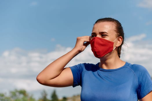 The determined athlete is getting ready for intense running on a sunny day while wearing a virus prevention mask on her face
