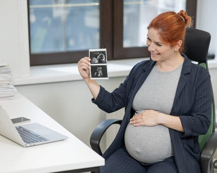 A pregnant woman shows a photo from an ultrasound scan of the fetus via video link in the office