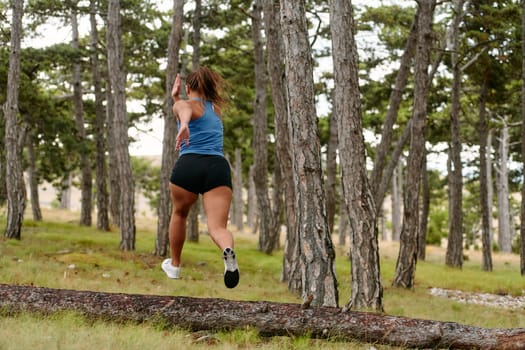 An intrepid woman fearlessly navigates through perilous forest terrain, effortlessly leaping over wooden obstacles with determination and grace, showcasing her adventurous spirit and athletic prowess