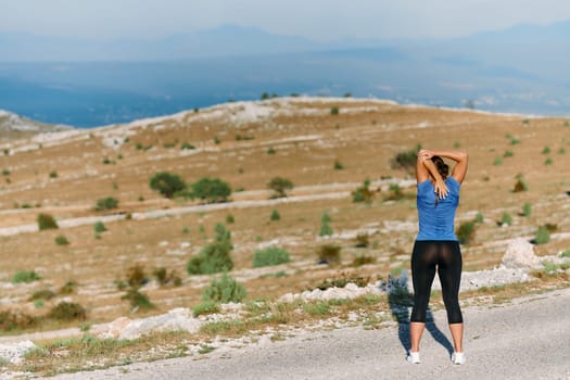 A determined female athlete stretches her muscles after a strenuous run through rugged mountain terrain, surrounded by breathtaking rocky landscapes.