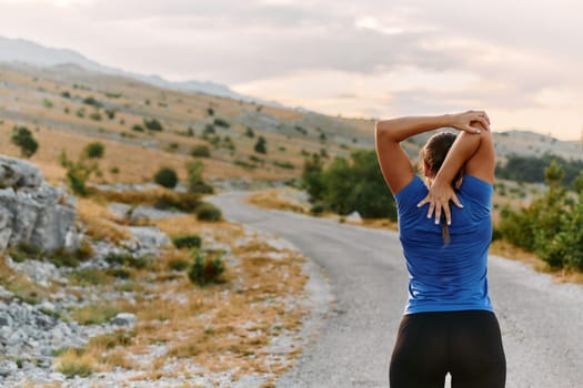 A determined female athlete stretches her muscles after a strenuous run through rugged mountain terrain, surrounded by breathtaking rocky landscapes.