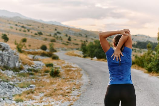 A determined female athlete stretches her muscles after a strenuous run through rugged mountain terrain, surrounded by breathtaking rocky landscapes.