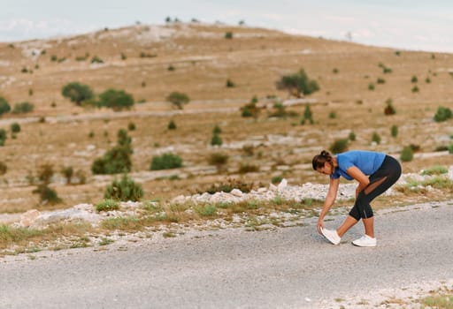 A determined female athlete stretches her muscles after a strenuous run through rugged mountain terrain, surrounded by breathtaking rocky landscapes.