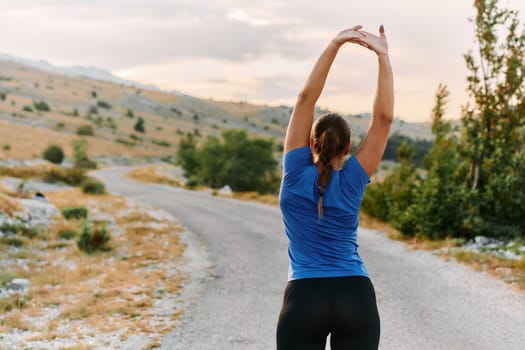 A determined female athlete stretches her muscles after a strenuous run through rugged mountain terrain, surrounded by breathtaking rocky landscapes.