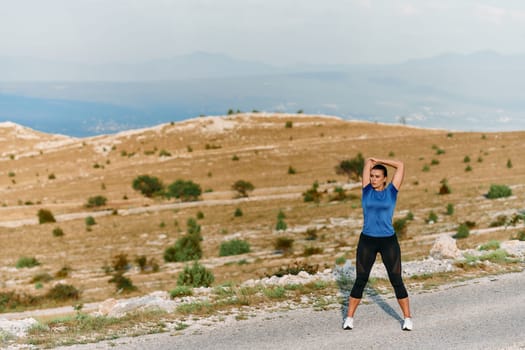 A determined female athlete stretches her muscles after a strenuous run through rugged mountain terrain, surrounded by breathtaking rocky landscapes.