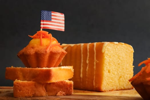 Carrot muffins, cake and cupcake on cutting board with american flag paper on black background, side view closeup. The concept of homemade cakes and carrot cake day.