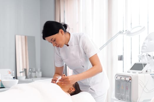 Cosmetologist wiping woman's face using antibacterial napkins. Doctor making beauty procedure in cosmetology clinic. Beautician cleaning face of patient in beauty clinic.