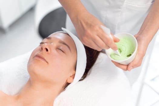 Beautician mixing creamy substance in bowl. Cosmetologist preparing alginate cream for relaxed woman lying in beauty salon. Spa and beauty treatment concept.