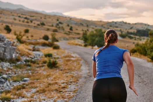 A determined female athlete runs through a forest trail at sunrise, surrounded by breathtaking natural beauty and vibrant greenery.