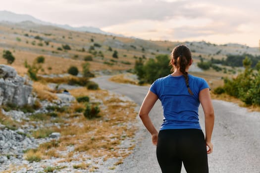 A determined female athlete stretches her muscles after a strenuous run through rugged mountain terrain, surrounded by breathtaking rocky landscapes.