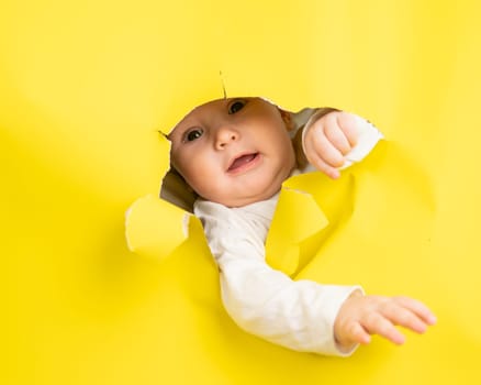 Cute Caucasian baby sticking out of a hole in a paper yellow background