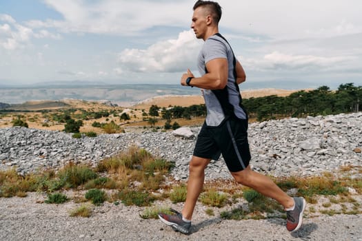 A muscular male athlete runs along a rugged mountain path at sunrise, surrounded by breathtaking rocky landscapes and natural beauty.