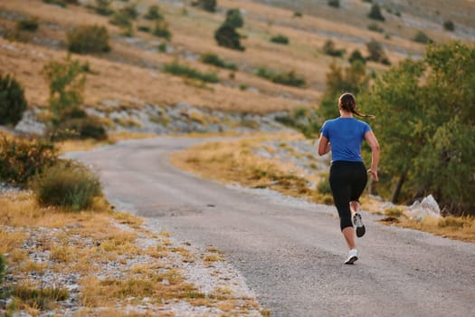 A determined female athlete runs through a forest trail at sunrise, surrounded by breathtaking natural beauty and vibrant greenery.