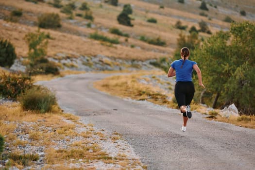 A determined female athlete runs through a forest trail at sunrise, surrounded by breathtaking natural beauty and vibrant greenery.