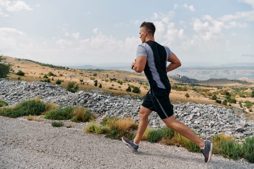 A muscular male athlete runs along a rugged mountain path at sunrise, surrounded by breathtaking rocky landscapes and natural beauty.